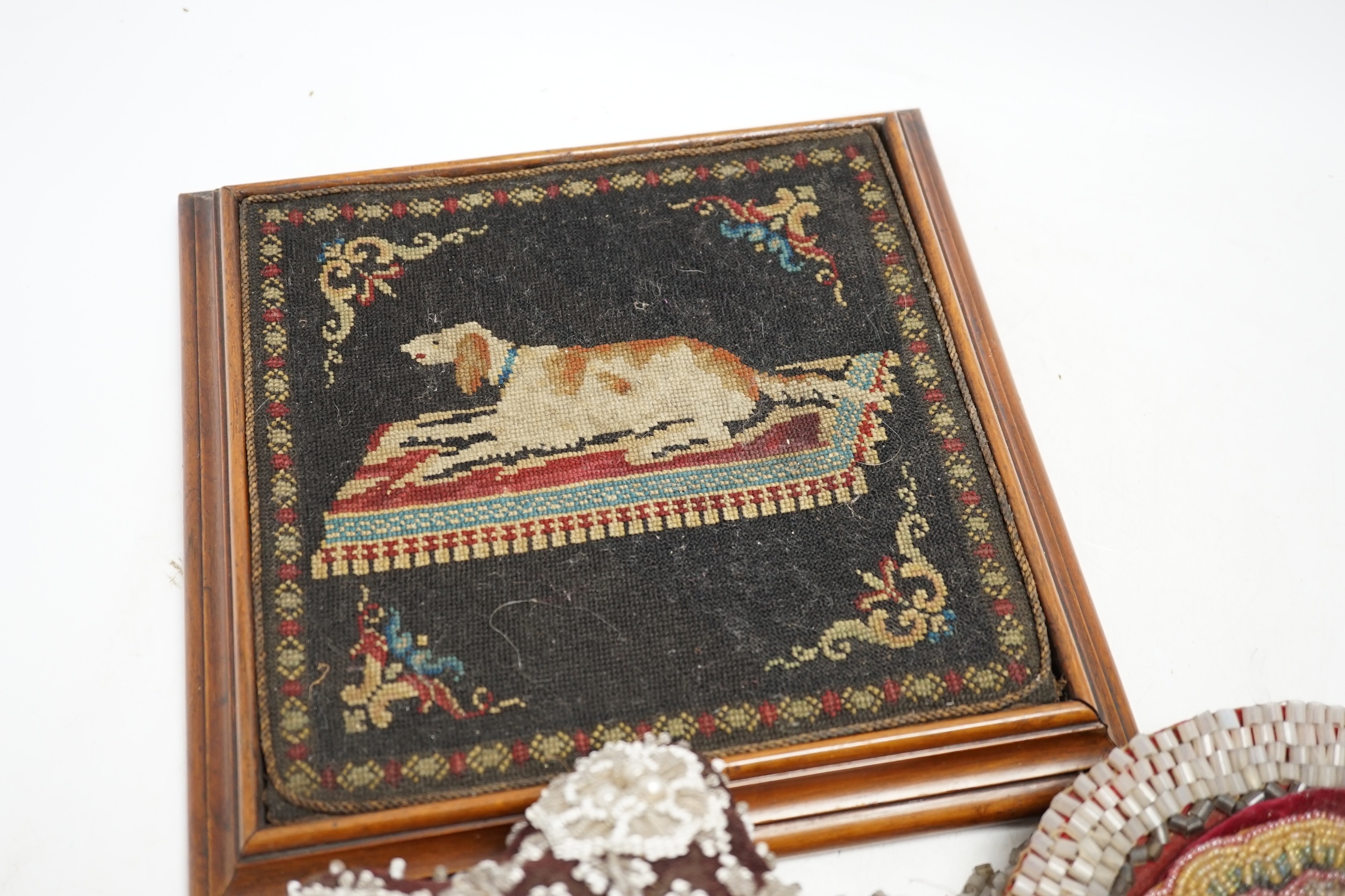 A 19th century framed needlework panel of a dog (possibly a teapot stand), a collection of bead worked mats, a beaded and tasselled tie-back and a large pin cushion, dog needlework 22.5cm wide. Condition - some beads mis